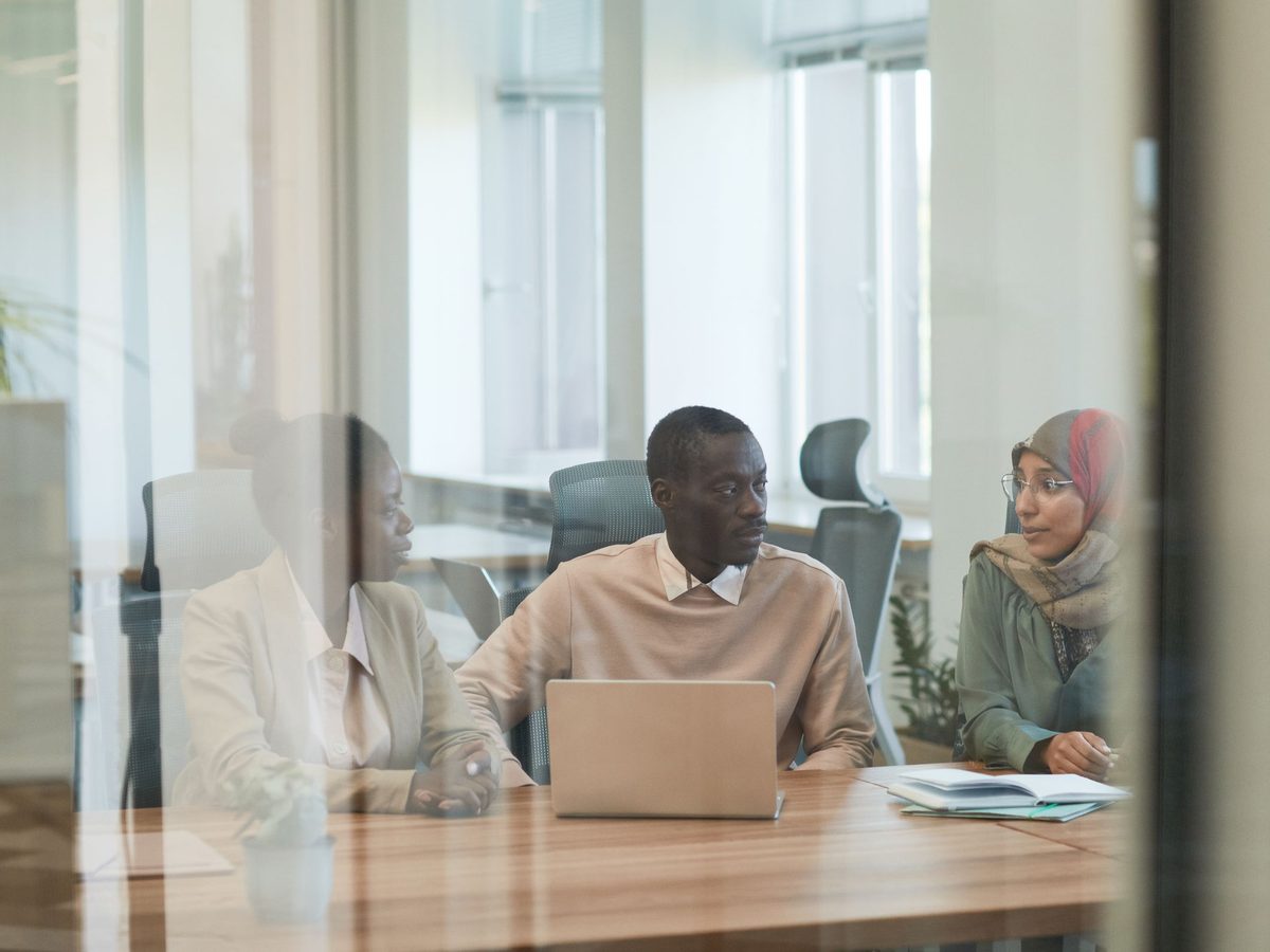 Three colleagues talking around a laptop, seen through a glass wall